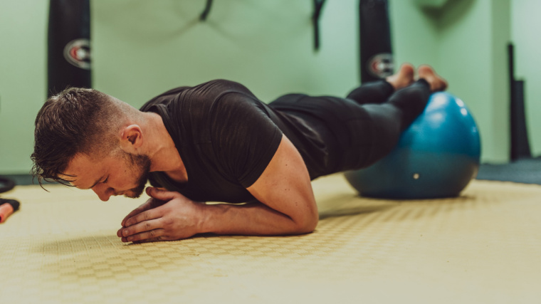 A person performs a plank with their feet on a stability ball.