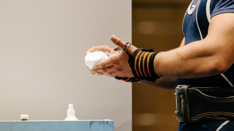 Person powdering their hands with chalk before attempting a lift with wrist wraps on