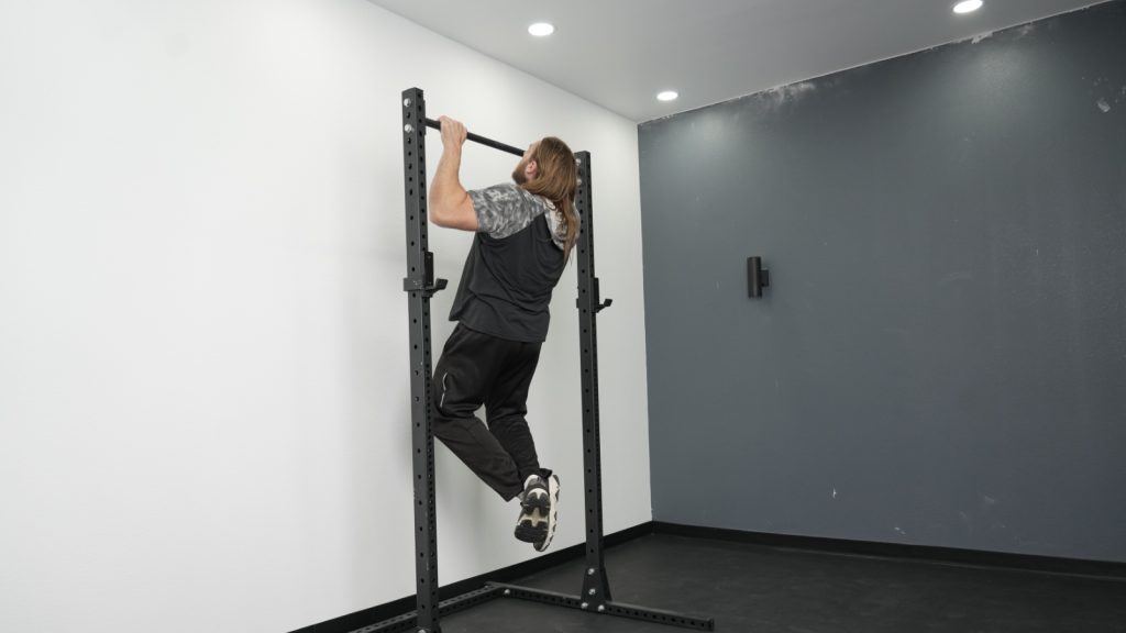 A person doing a pull-up on the Fringe Sport Unlimited Squat Stand with Pull-Up Bar.