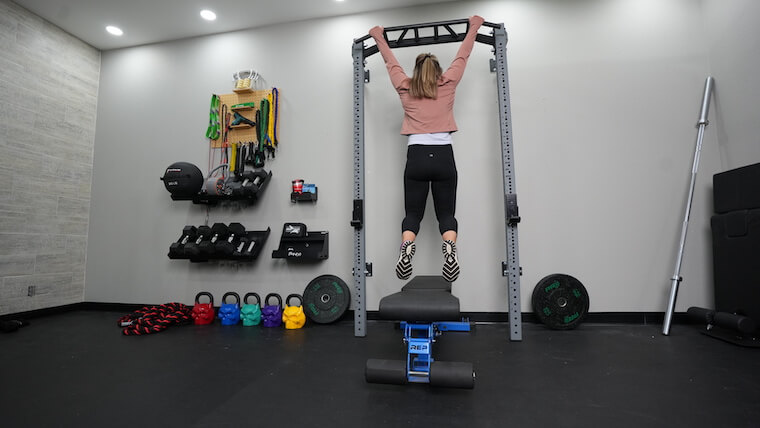 A person hanging from the Profile Pro Folding Squat Rack.