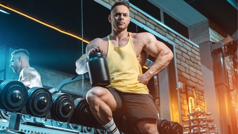 A bodybuilder holding a container of supplement powder.