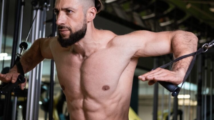 A muscular person working out with cables.