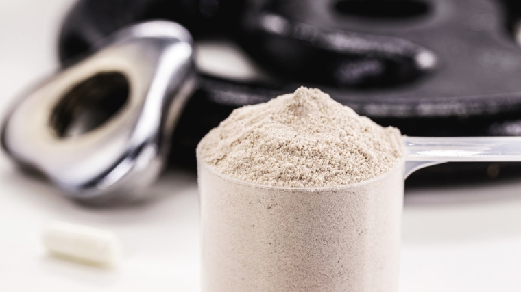 A scoop of creatine with weights in the background.