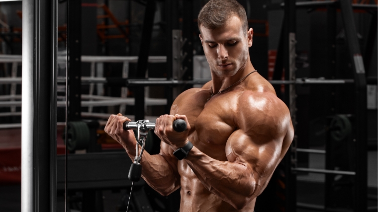 A shirtless bodybuilder doing cable biceps curls.