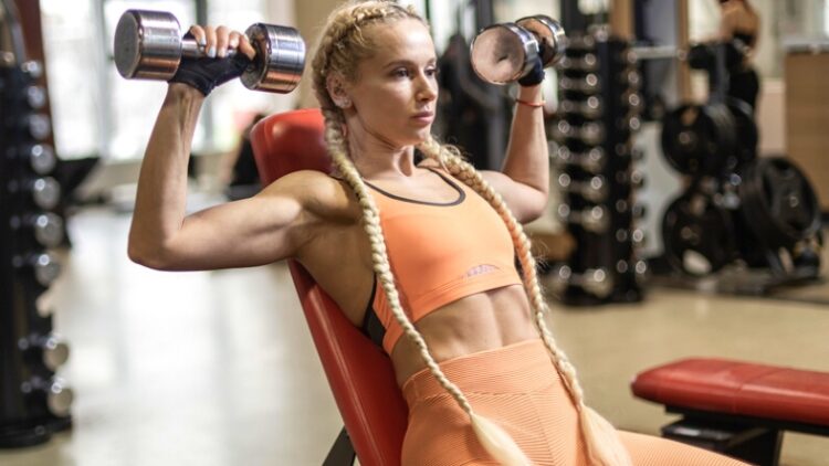 A person holding dumbbells over their shoulders and leaning back.