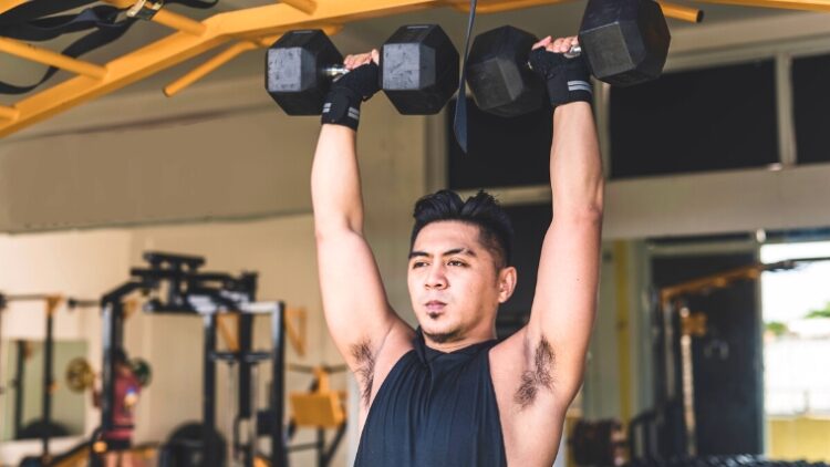A person holding dumbbells over their shoulders with their arms straight up.