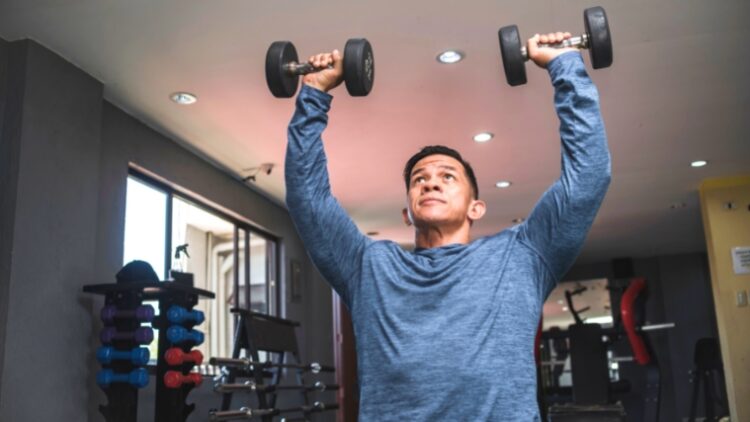 A person holding dumbbells over their shoulders without locking their elbows.