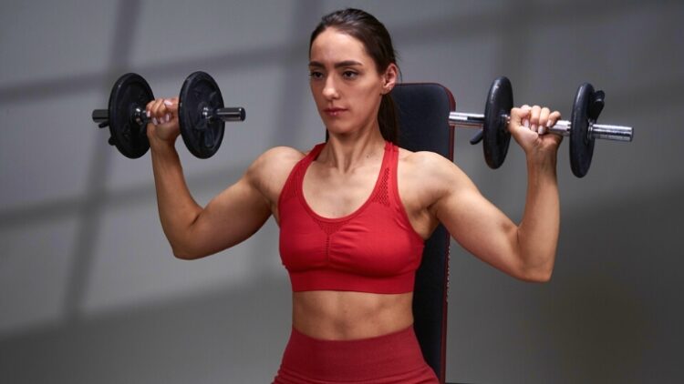 A person with muscular shoulders doing the dumbbell shoulder press.