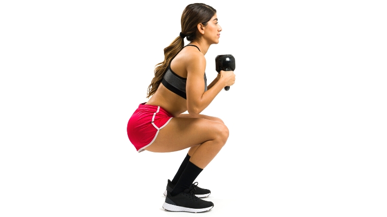 A person doing a kettlebell goblet squat, ascending from a deep squat.