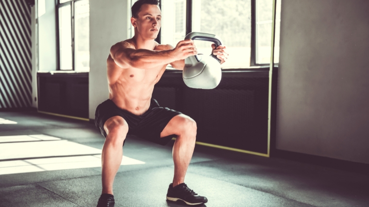 A person doing a kettlebell goblet squat, holding it away from their chest.