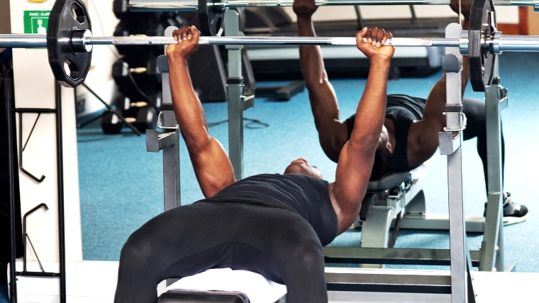 A person performing a barbell bench press next to a mirror.