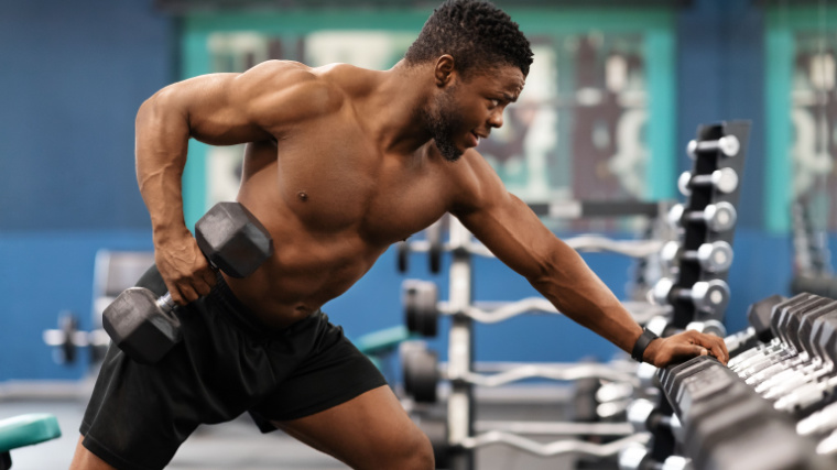 Man performs dumbbell row while leaning against weight rack