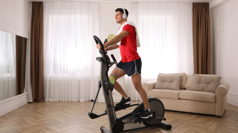 person exercising on an elliptical with headphones and a towel in red shirt and black shorts