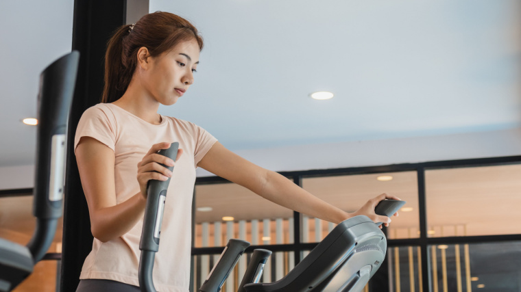 Person exercising on an elliptical machine with a peach shirt
