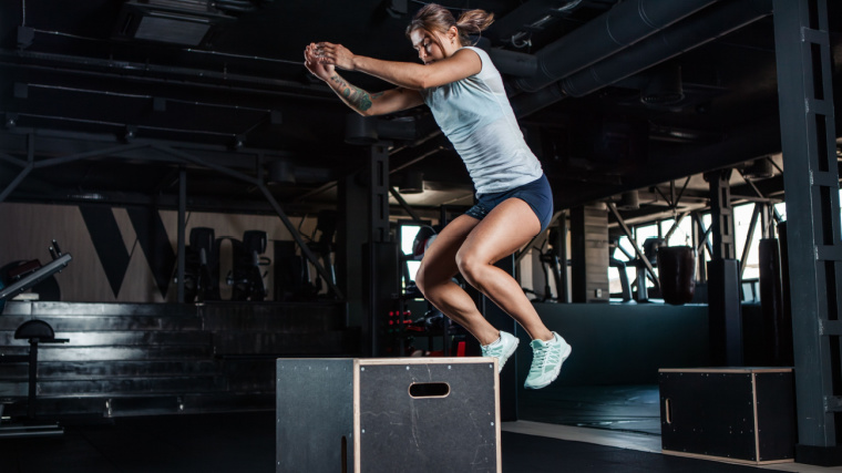 Person jumping onot black wooden plyometric box in gym