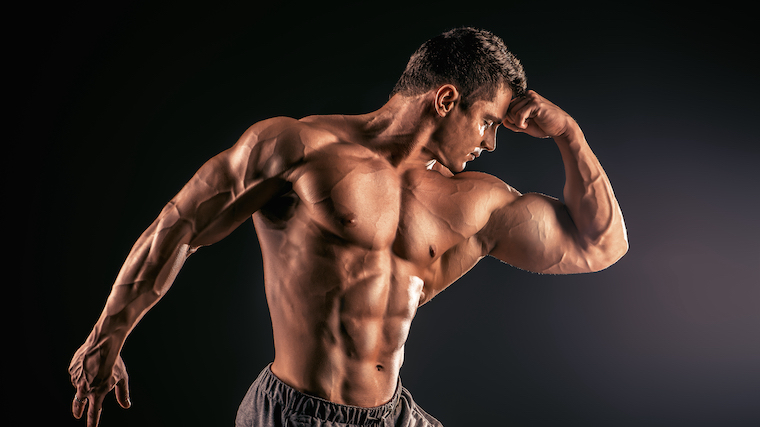 Muscular bodybuilder posing against a black background, placing his head into his closed fist to create a pensive pose.