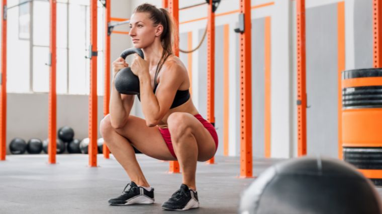 Person in a black tank top and red shorts performing a goblet squat by holding a kettlebell at chest level.