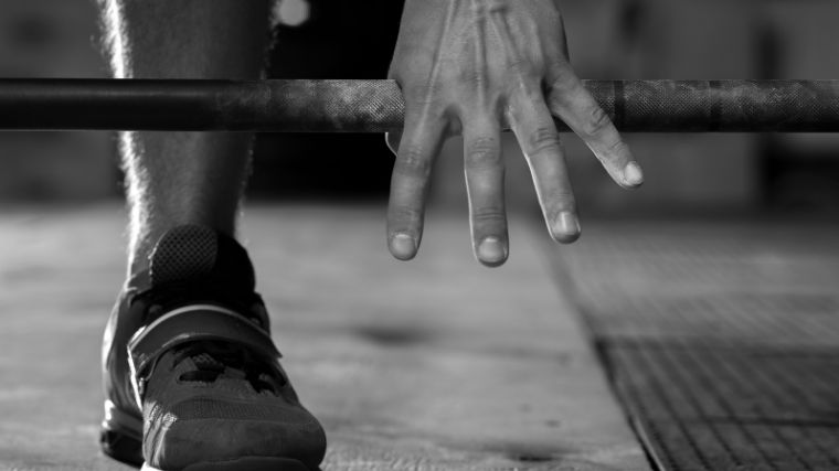 A close-up black and white photo of a hand gripping a barbell.