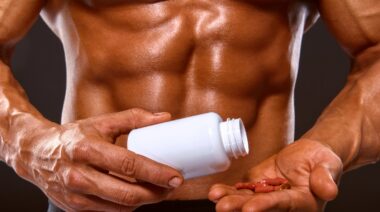 A muscular person holding supplement capsules.