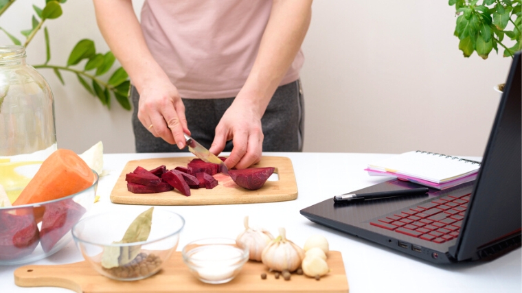 A person slicing beets, and using a laptop.