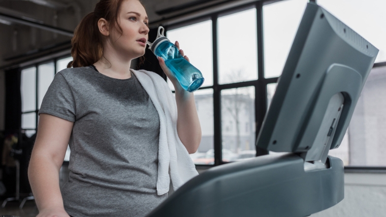 A person sweating on the treadmill, drinking water.