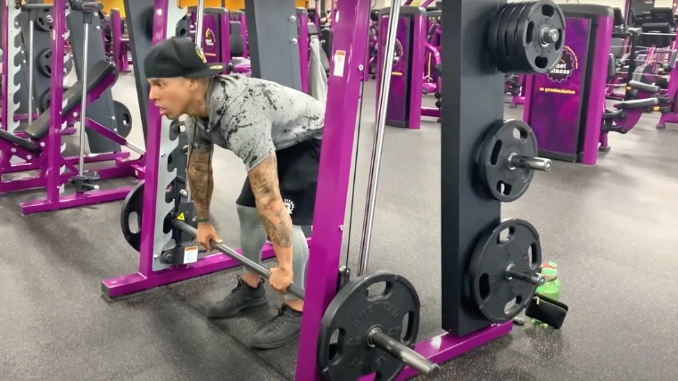 A person with an unracked bar on a Smith machine.