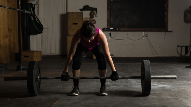 A woman hinging at the hips to lift a barbell.
