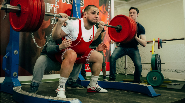 Powerlifter squats a heavy weight with spotters