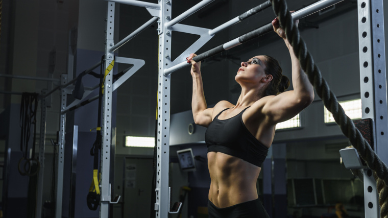 An athlete wearing make-up and a sports bra performs a pull-up.