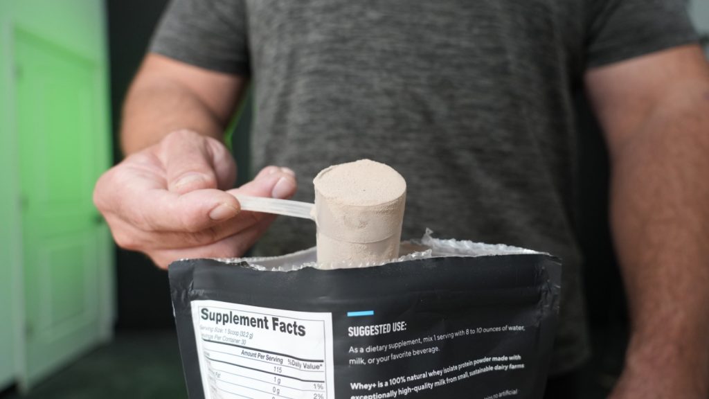 A person holds a scoop of Legion Whey+ protein powder