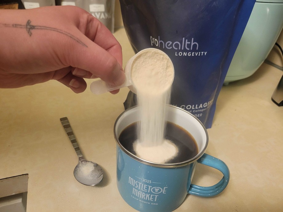 Pouring a scoop of Pro Health Longevity Collagen into a cup of coffee.