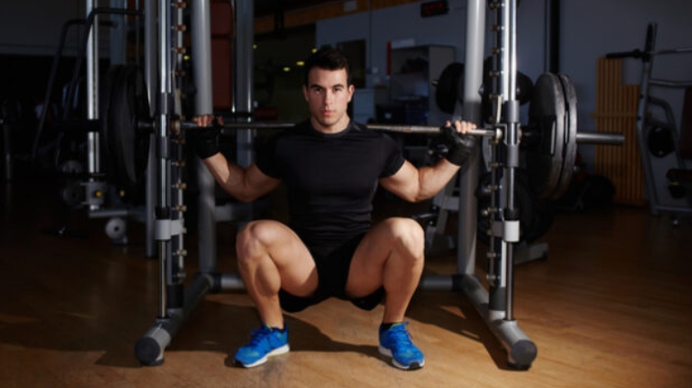 A bodybuilder doing a back squat using a machine.