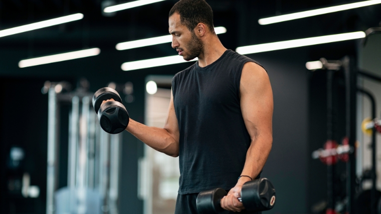 Concentrated man doing dumbbell workout. Well trained body with bulky  muscles. Sport equipment and weightlifting. Stock Photo