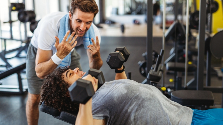 A person working out using dumbbells with a gym partner.