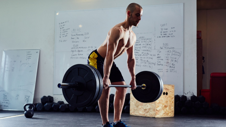 Shirtless man pushes with legs while performing clean exercise