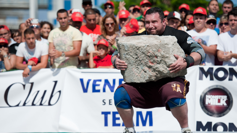 A strongman athlete carries a lifts a stone in outdoor competition.