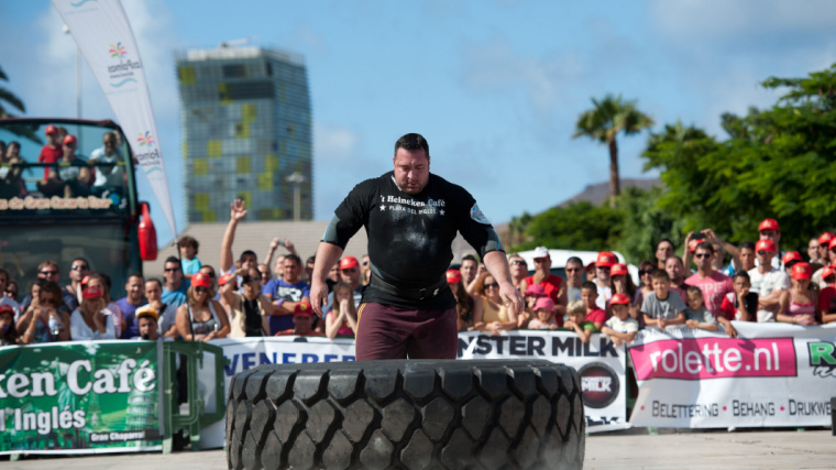 A strongman athlete performs a tire flip in front of a crowd.