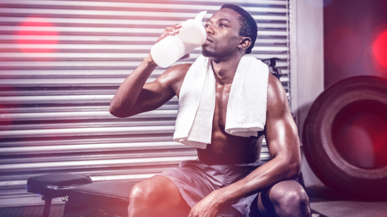 A shirtless athlete drinks pre-workout before a training session.