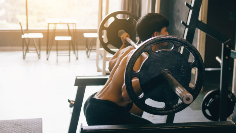 A shirtless powerlifter performs a barbell squat.