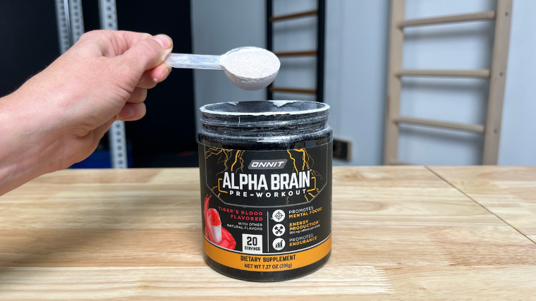 A person lifts out a scoop of Onnit Alpha-BRAIN Pre-Workout from the jug.