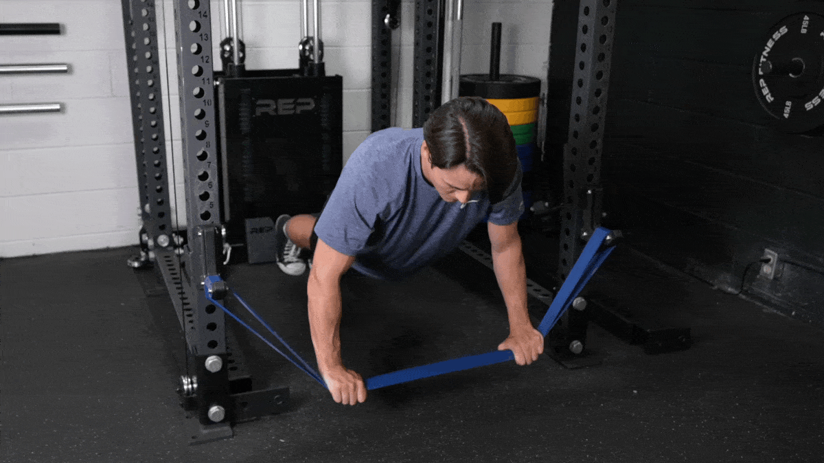 A person performing the chaos push-up with the power rack and resistance band in the Barbend gym.