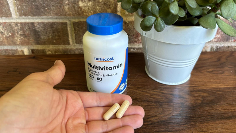 A hand holding two Nutricost Multivitamin capsules.