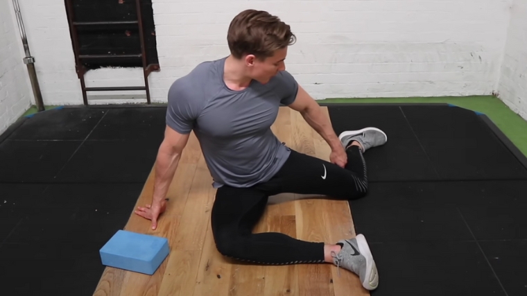 A muscular person setting up their back leg for the 90/90 stretch.