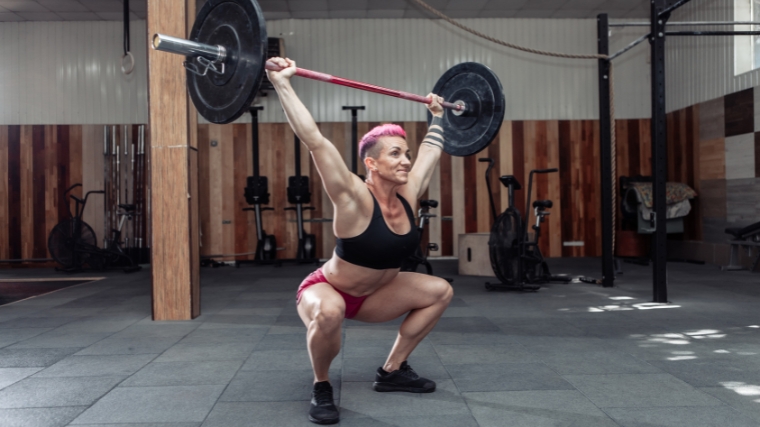 A person in a black sports bra and pink shorts doing an overhead squat.