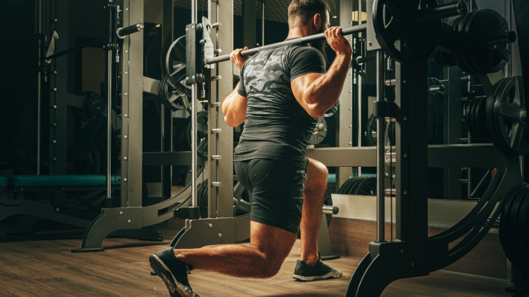 A muscular person doing the Smith machine split squat.
