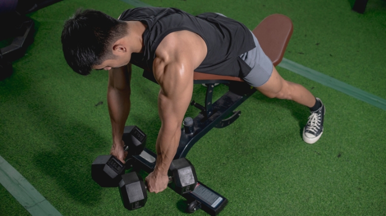 A muscular person starting to do the chest-supported dumbbells rows.