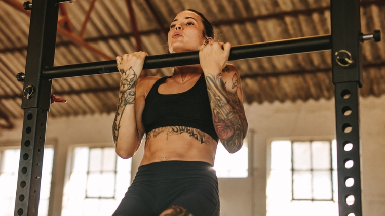 A person with tattoos doing chin-ups in the gym.