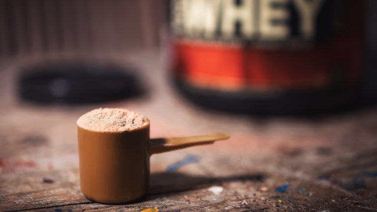 A scoop of whey protein powder and the container in the background.