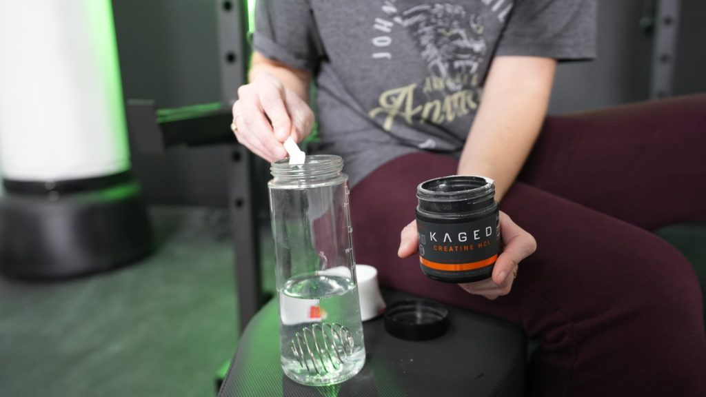 A BarBend tester putting a scoop of Kaged Creatine HCl into a shaker bottle.