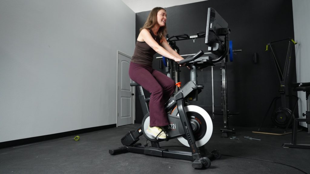 A woman is shown riding the NordicTrack S22i exercise bike